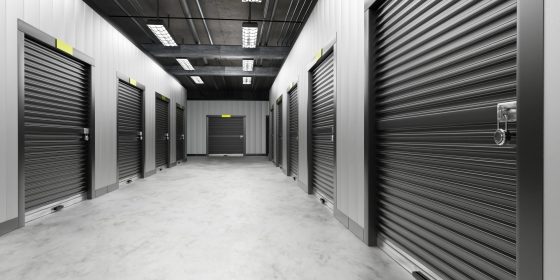Self-stockage. Couloirs d’entrepôt avec portes noires. Les portes du self-stockage sont fermées. Intérieur du bâtiment d’entrepôt. Visualisation hangar avec grand self stockage. Serrurerie industrielle avec cadenas